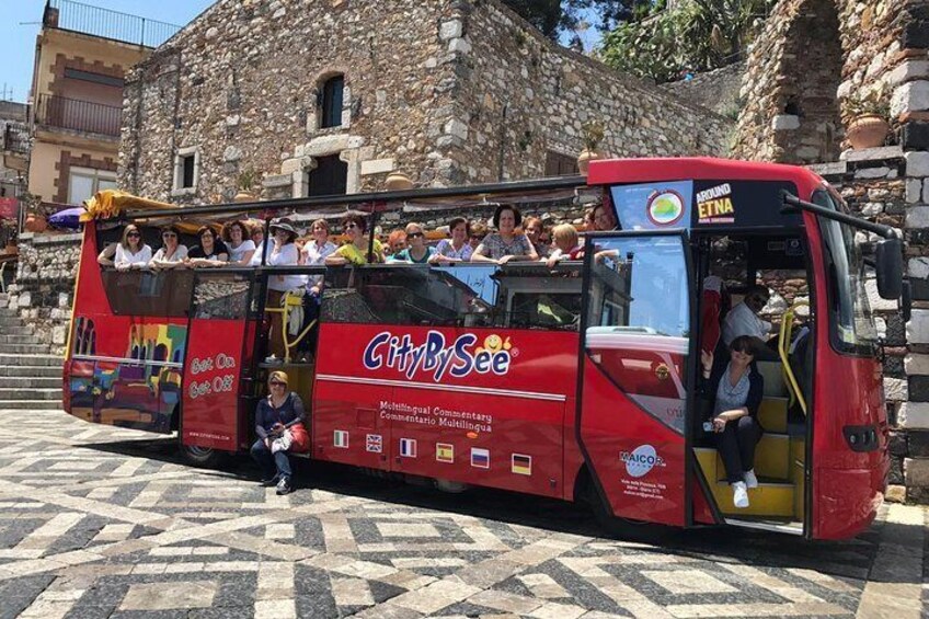 A red CityBus with passengers, parked in front of a stone building. 4