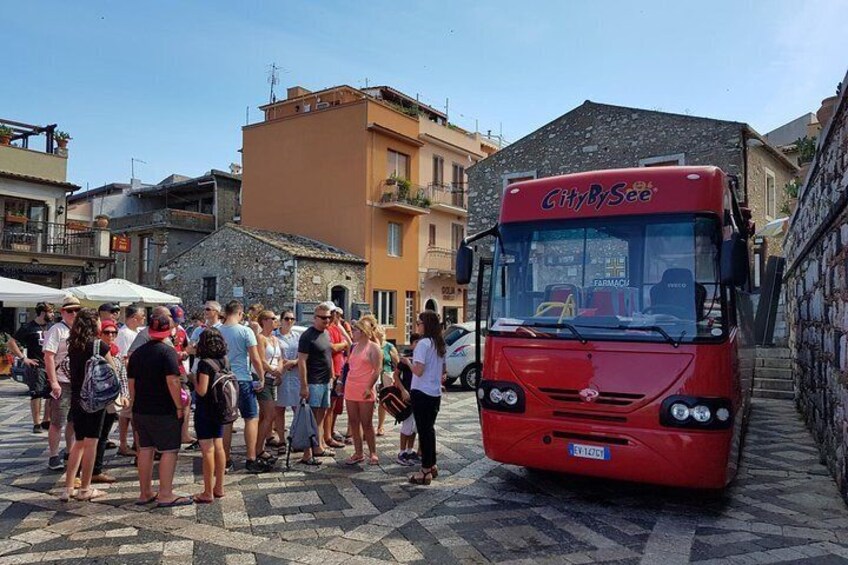 A red CityBySee bus parked on a cobblestone street with people standing around it. 5