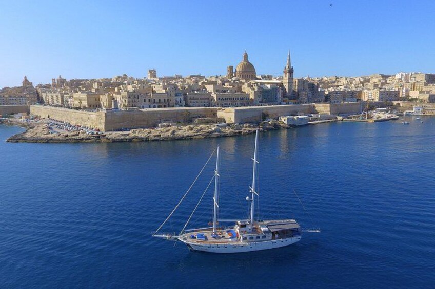 A sailboat on calm waters, a historic cityscape with prominent buildings, and a clear blue sky. 2
