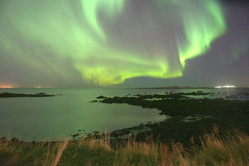 The Northern Lights over a calm body of water with distant lights on the horizon. 2