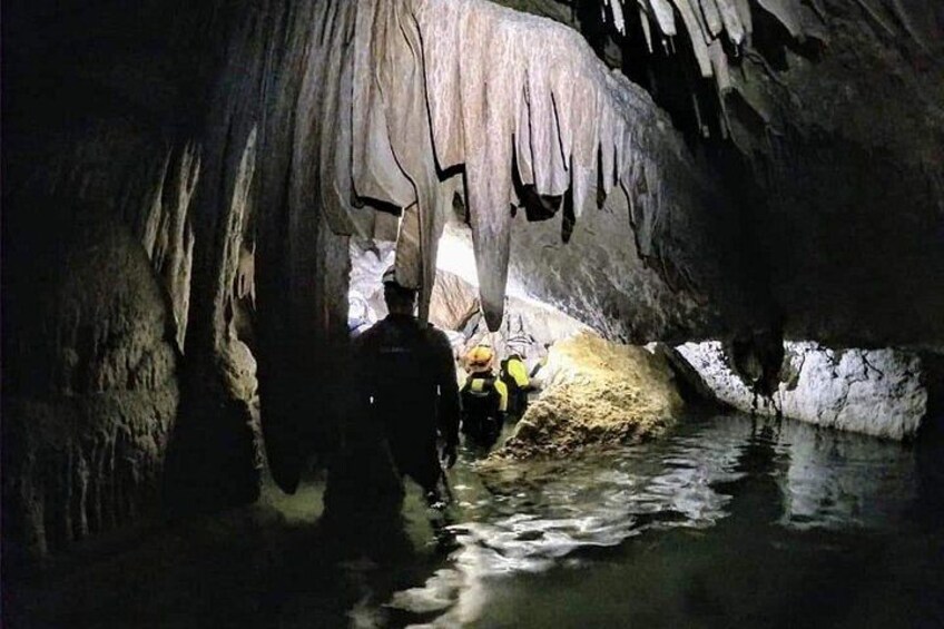 A cave with stalactites and stalagmites, a person in a yellow vest, and water. 3