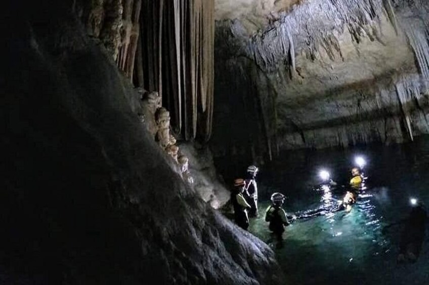 A cave with stalactites and stalagmites, a group of people exploring, and a water body. 4