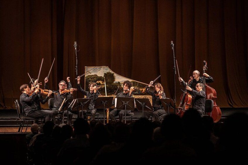 A string quartet performing on stage with a backdrop of a painting. 3