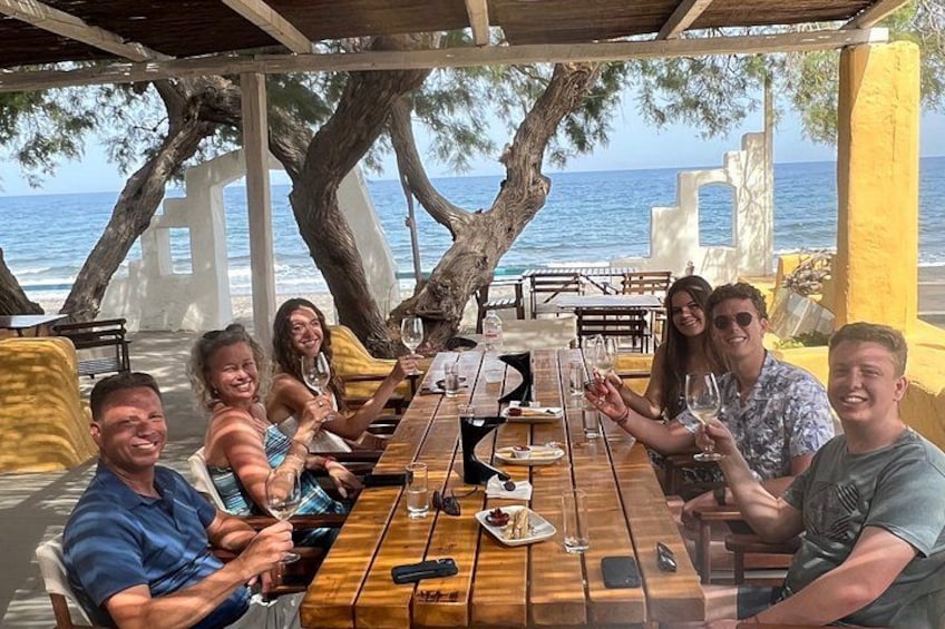 Un grupo de personas cenando en una mesa de madera con vista al océano. 2