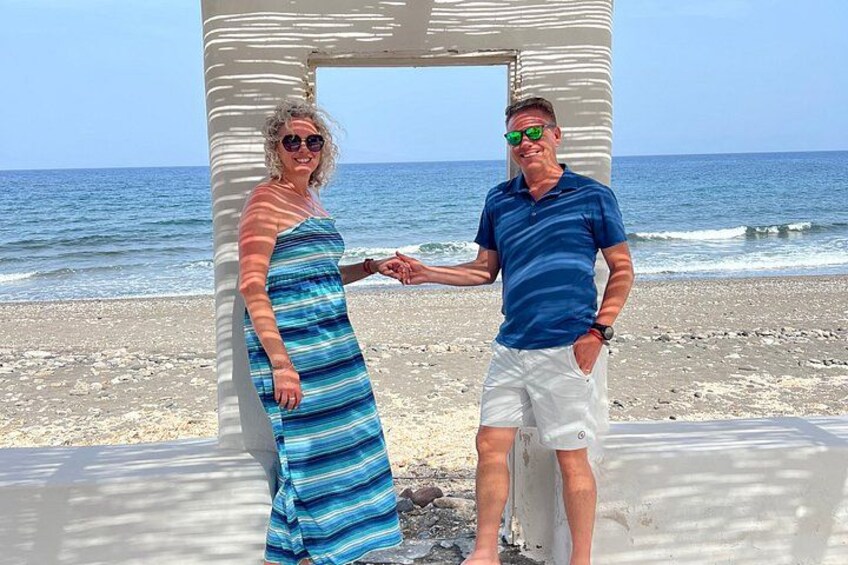 Dos personas tomadas de la mano en una playa, con un cielo despejado y el océano al fondo. 3
