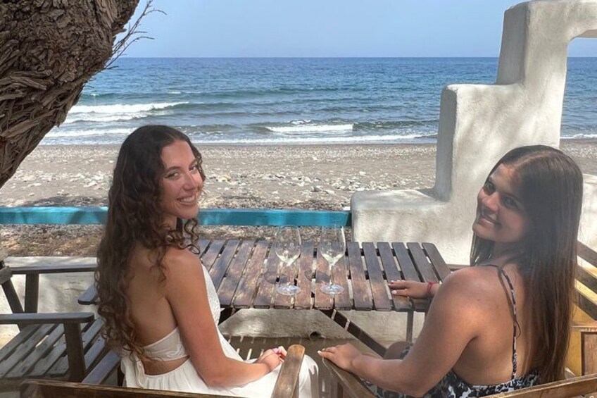 Dos personas sentadas a una mesa de madera junto a la playa, con una gran escultura de concreto al fondo. 5