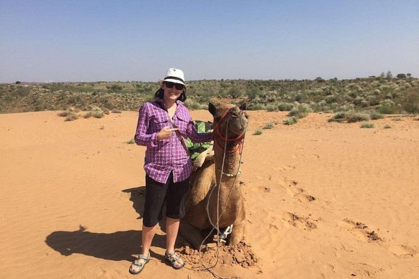 A person standing next to a camel in a desert with sparse vegetation. 4