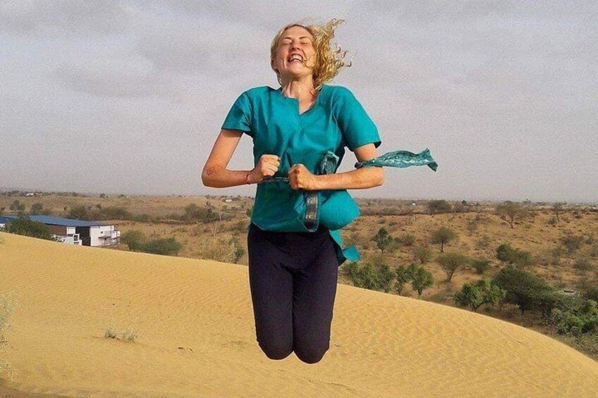 A person jumping in a desert landscape with sand dunes and sparse vegetation. 2