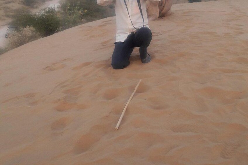 A person kneeling on a sandy surface with a stick in front of them. 5