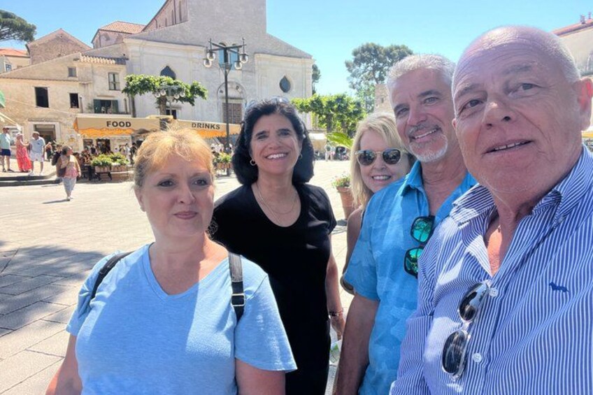 Eine Gruppe von Menschen steht auf einem öffentlichen Platz, im Hintergrund sind Gebäude und Geschäfte zu sehen. 2