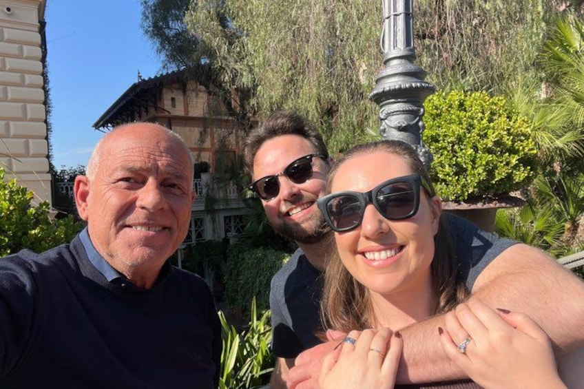 Three people posing outdoors with a building and greenery in the background. 2