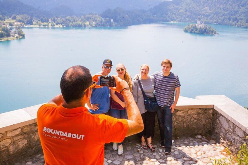 A group of people standing on a stone platform overlooking a lake with a photographer in an orange shirt. 3
