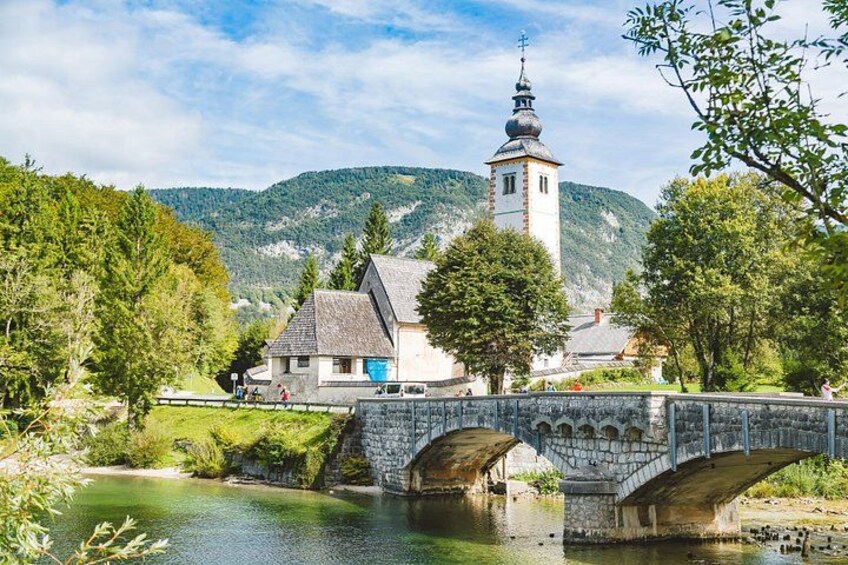 Een stenen brug over een rivier, een kerk met een klokkentoren en een bergachtig landschap. 5