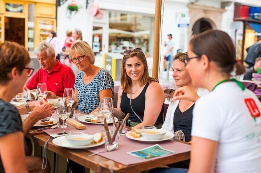 A group of people dining at an outdoor restaurant with tables set with plates, glasses, and cutlery. 4