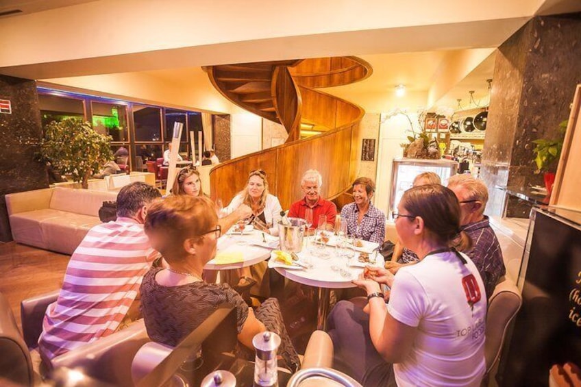 A group of people sitting around a round table in a modern indoor setting with wooden accents and plants. 5