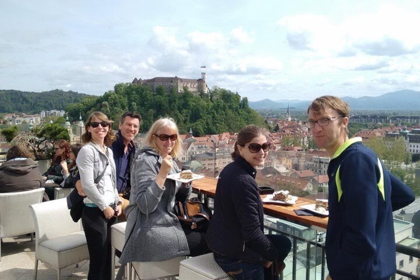 A group of people on a rooftop terrace overlooking a city with a hill and castle in the background. 5