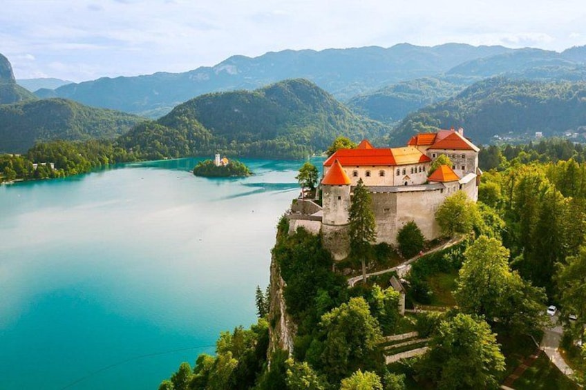 A castle on a cliff overlooking a turquoise lake surrounded by lush green hills. 5