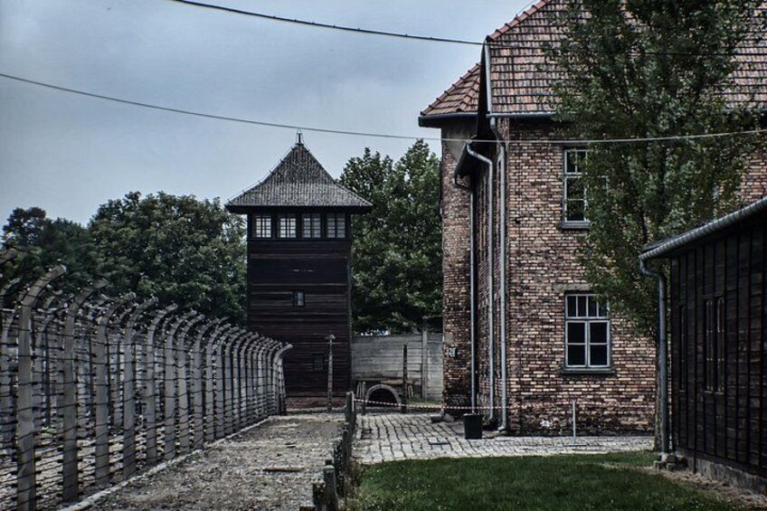 A brick building with a tower, a fence, and a paved area. 3