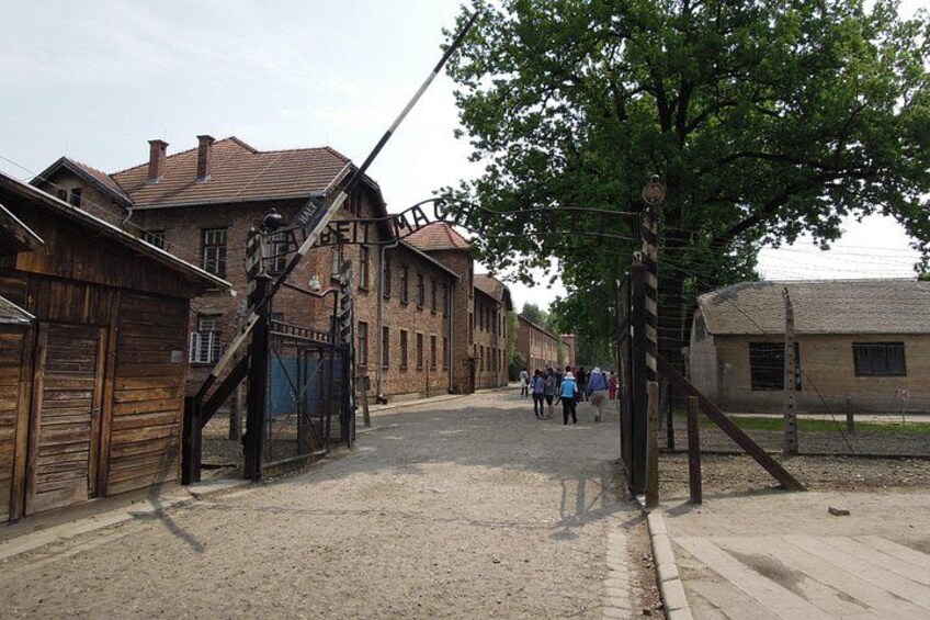 A historical site with old wooden buildings, a metal gate, and a paved pathway. 4