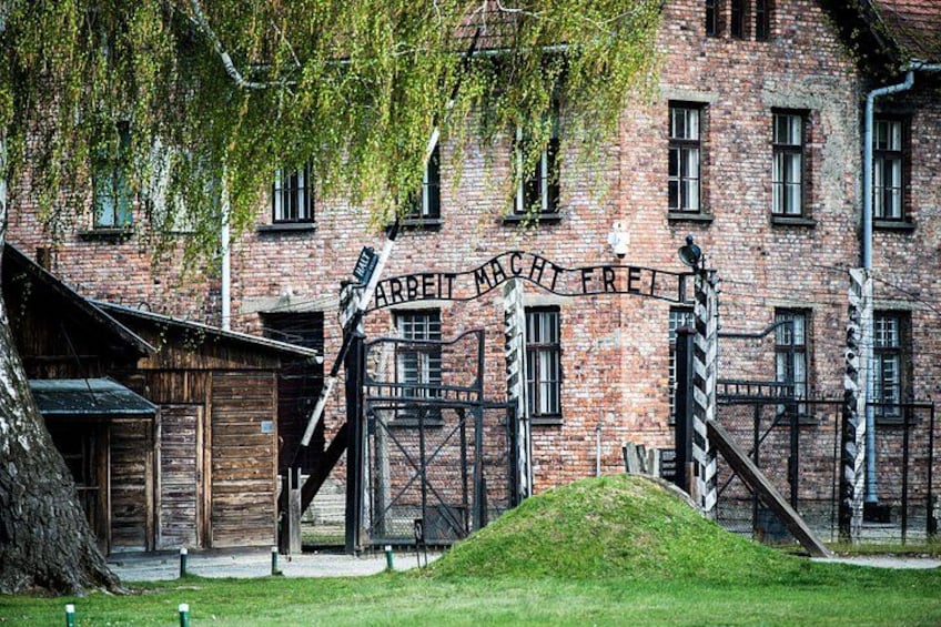 A historic building with a sign reading 'ARBEIT MACHT FREI' and a wooden structure to the left. 1