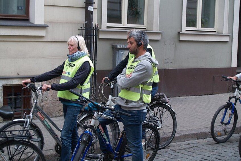 Zwei Personen in Warnwesten stehen neben Fahrrädern auf einer Kopfsteinpflasterstraße. 2