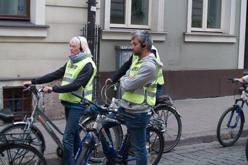 Dos personas con chalecos de seguridad de pie junto a bicicletas en una calle empedrada. 2