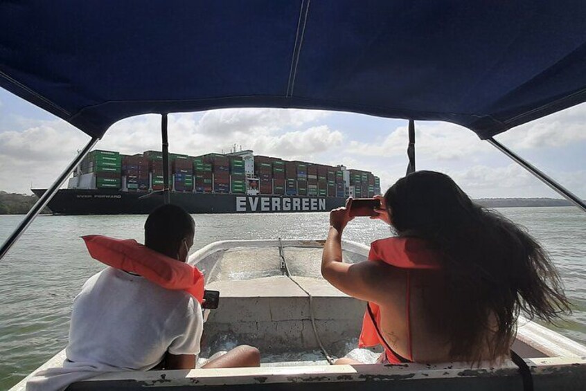 Two people on a boat with a large container ship labeled 'EVERGREEN' in the background. 1