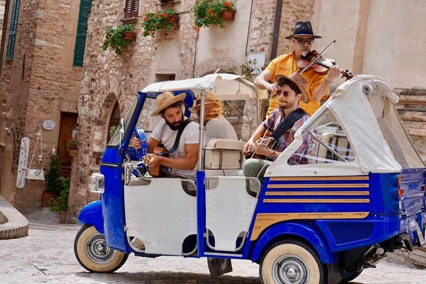 A blue and white vintage car with two passengers, one playing a violin and the other holding a camera. 4