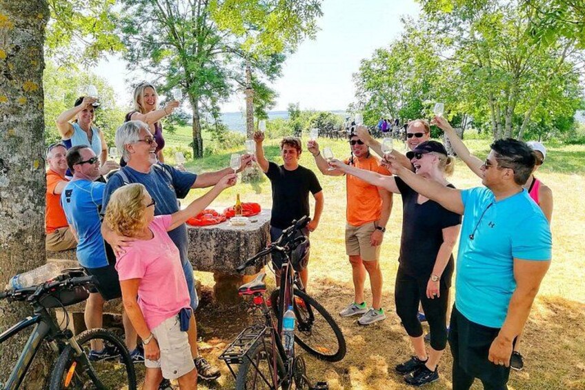 A group of people around a table with a red cloth, bicycles, and trees in the background. 2