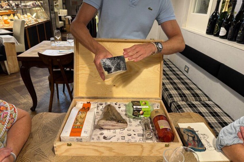 A person opening a wooden box containing various food items and a bottle of wine. 2