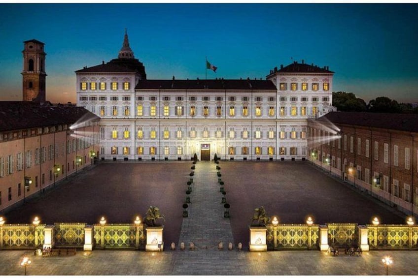 A large, illuminated building with a symmetrical facade, a central entrance, and a courtyard with a fountain. 3
