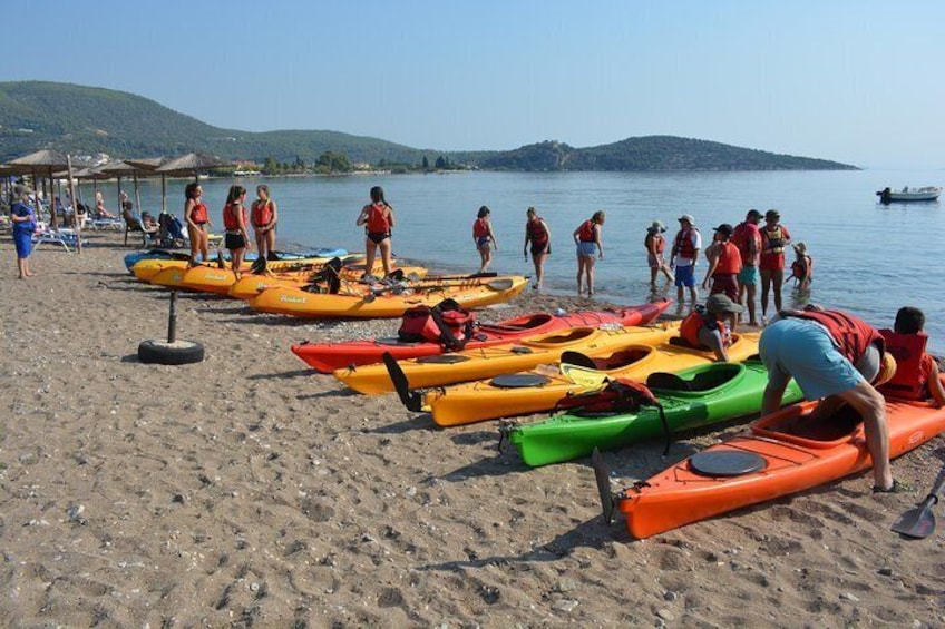 People preparing kayaks on a beach with a lake and hills in the background. 3