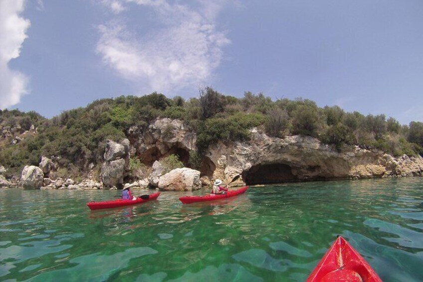 Three red kayaks on clear water with a rocky coastline and a cave entrance in the background. 5