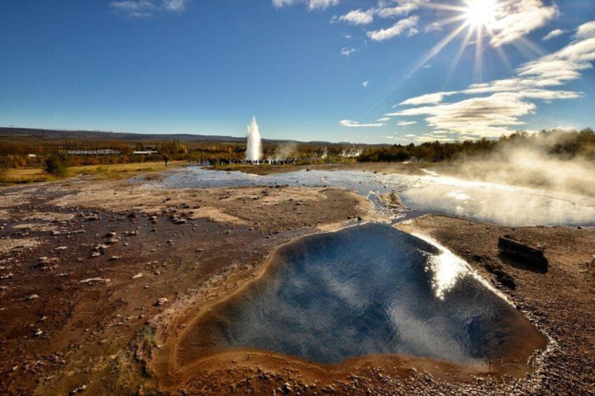 A geothermal area with a hot spring, steam, and a geyser. 4