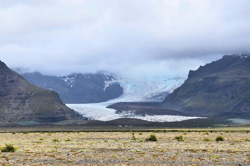 A glacier between mountains, a glacier in the valley, and a cloudy sky. 3