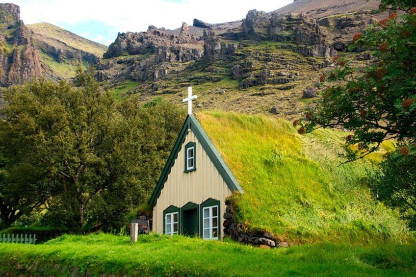 A small church with a cross on top, surrounded by lush greenery and rocky hills. 5