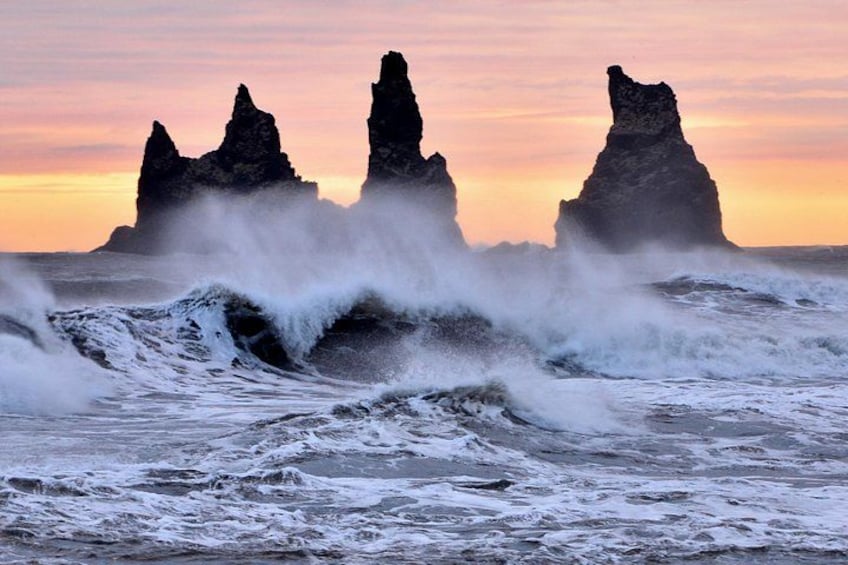 A coastal scene with waves crashing against rock formations during sunset. 2