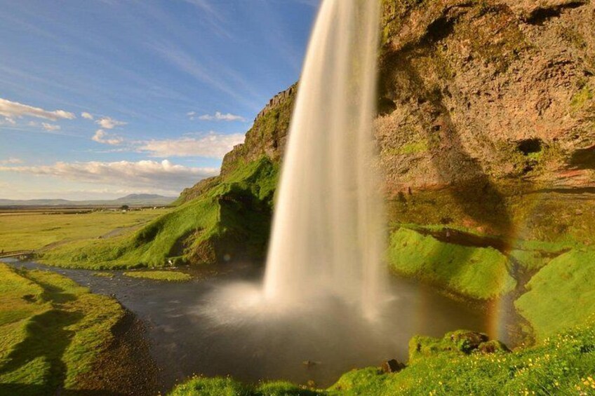 A waterfall cascading down a cliff into a river, surrounded by green grass and a clear sky. 4