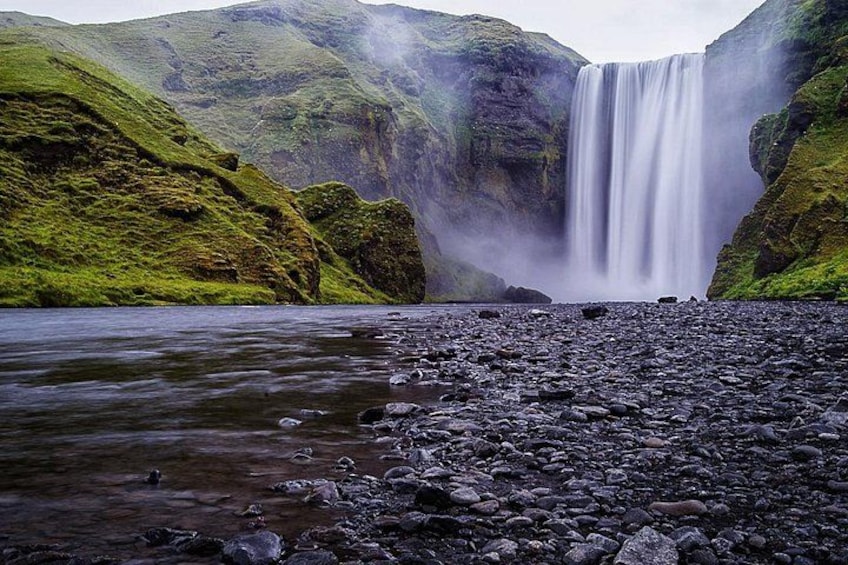 A waterfall, rocky riverbed, and lush green hills. 2