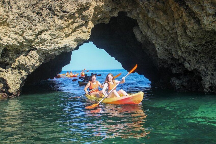 People kayaking through a natural rock arch formation. 3