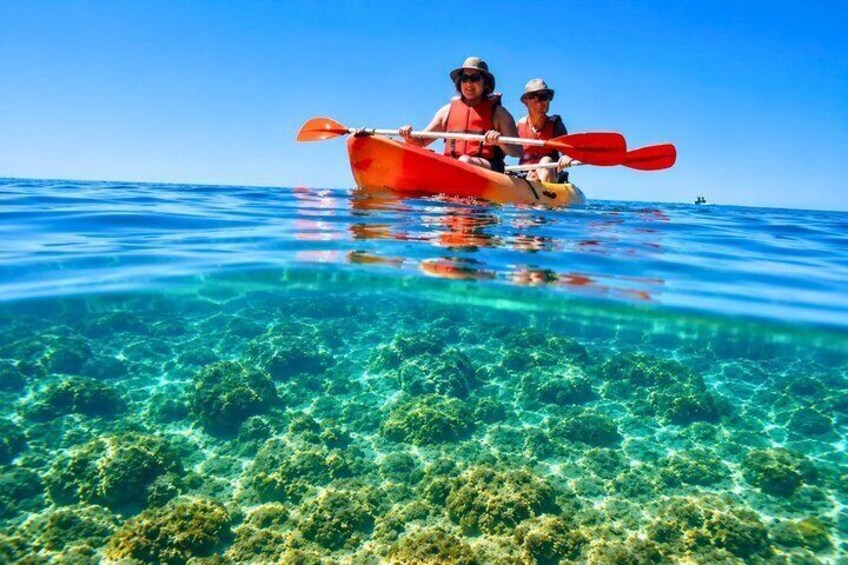 Two people kayaking on clear blue water with visible underwater coral. 1