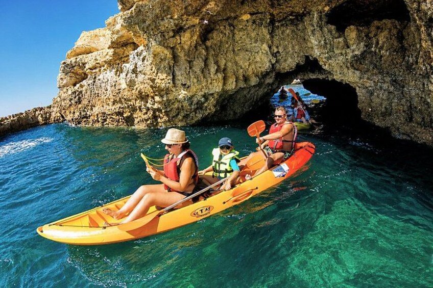 Two people kayaking on clear blue water with a rocky cliff in the background. 5