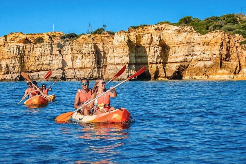 People kayaking on a calm sea with rocky cliffs in the background. 4