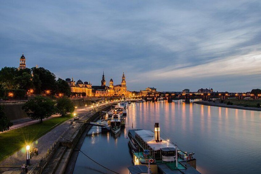 A river with a boat docked, a bridge, and illuminated buildings in the background. 3