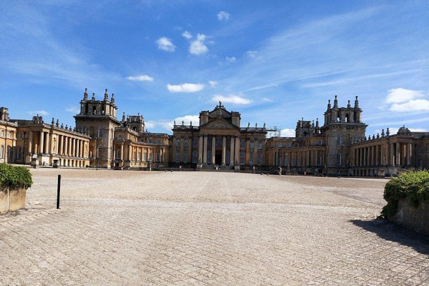 En stor, historisk byggnad med klassisk arkitektur, en stenlagd innergård och en klarblå himmel. 2