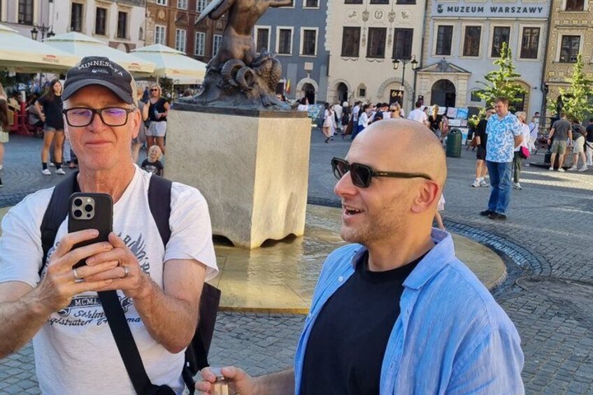 Two people taking a selfie in a public square with a statue and a building labeled 'Muzeum Warszawy' in the background. 5