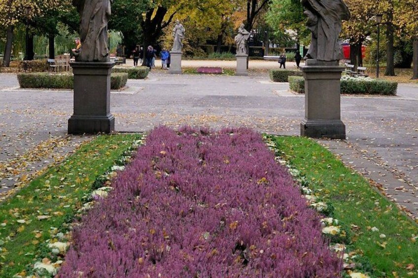A park with a central flower bed, statues, and a paved walkway. 4