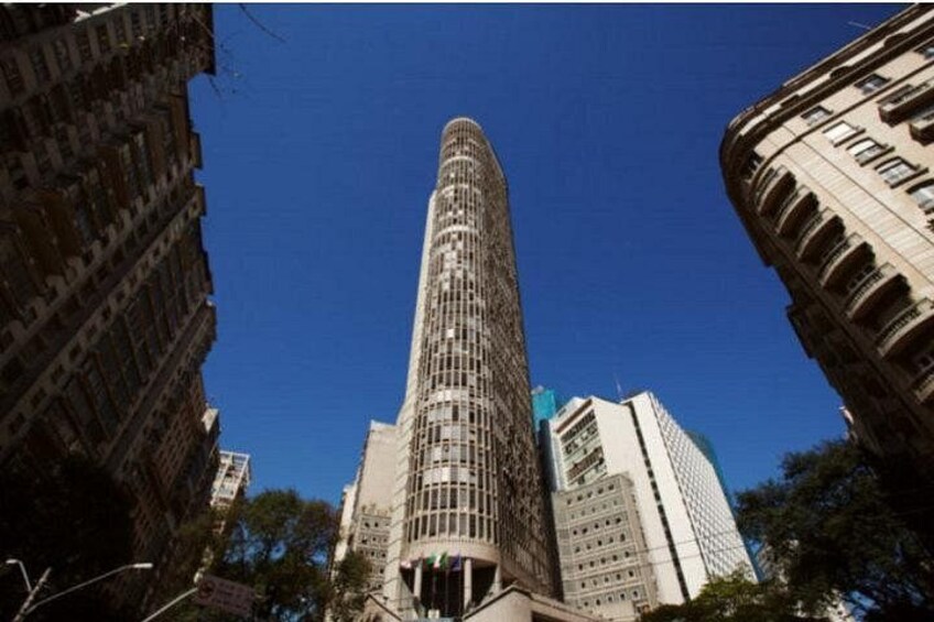 Un edificio alto y cilíndrico con fachada de entramado, rodeado de otros edificios de gran altura. 2