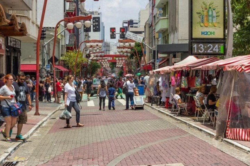 Una calle concurrida con peatones, puestos de mercado y un reloj marcando 13:24. 4