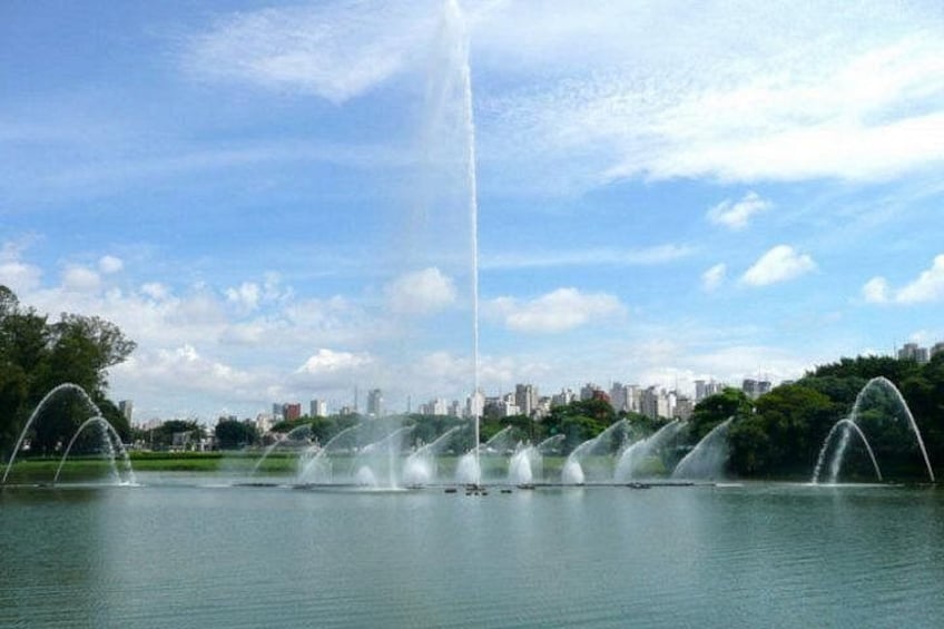A fountain with multiple streams in a park with a city skyline in the background. 2